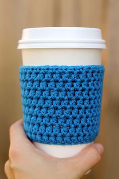 a hand holding a coffee cup with a crochet pattern on the sleeve and bottom