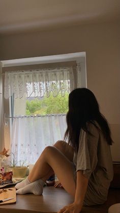 a woman sitting on top of a wooden counter next to a window with curtains behind her