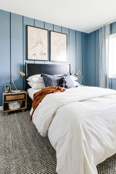 a bedroom with blue walls and white linens on the bed, two pictures above the bed