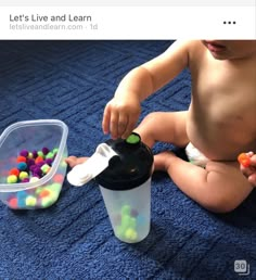 a baby sitting on the floor next to a cup filled with gumballs and playing with it