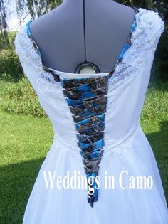 the back of a wedding dress with blue and white ribbons on it, in front of grass