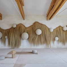 an art installation with balls and grass hanging from the ceiling, in front of a white wall