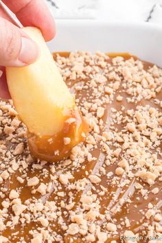 a person dipping an apple into a bowl of caramel sauce with crumbs