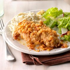 a white plate topped with chicken, mashed potatoes and lettuce next to a fork