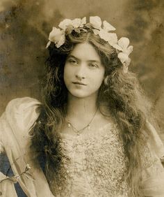 an old photo of a young woman with long hair and flowers in her hair,