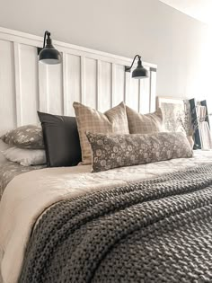 a bed with many pillows on it and two lamps above the headboard, in a bedroom