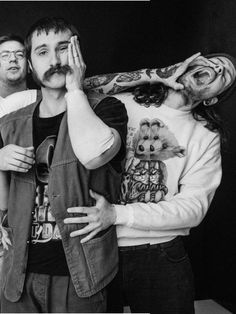 two men are standing next to each other with tattoos on their arms and shoulders, one is covering his eyes