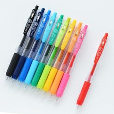 several different colored pens lined up next to each other on a white surface with one pen in the middle