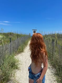 a woman with red hair walking down a sandy path to the beach on a sunny day