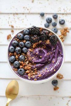 a bowl filled with blueberries and granola on top of a white table next to a spoon