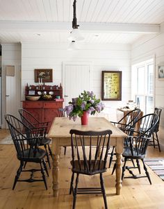 a dining room table with chairs and a vase on it's centerpiece, in front of a white paneled wall