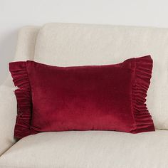 a white couch with a red pillow on it's back and two pillows sitting next to it