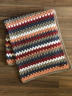 a multicolored crocheted blanket laying on top of a wooden floor