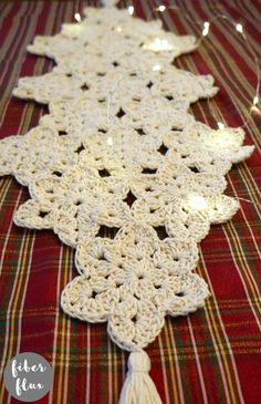 a crocheted table runner with tassels and lights in the background on a plaid cloth