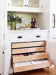 a kitchen with white cabinets and drawers filled with wine bottles, glasses and other items