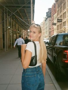 a woman with long blonde hair standing next to a black truck on the side walk