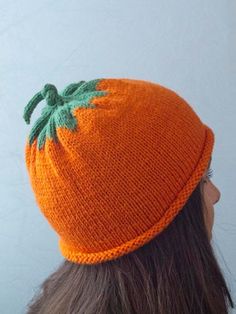 a woman wearing an orange knitted hat with a green leaf on the top and bottom