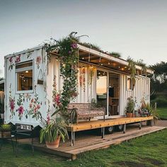 a tiny house made out of shipping containers with flowers on the side and plants growing outside