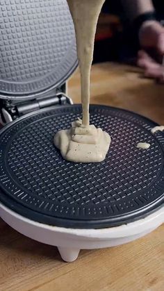 a person is pouring sauce on top of a waffle maker that's sitting on a table