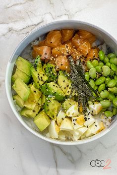 a bowl filled with vegetables and rice on top of a marble countertop next to a spoon