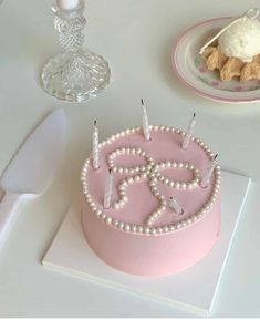 a pink birthday cake with white frosting and candles on a table next to other desserts