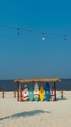 surfboards are lined up on the beach under a straw hut that is built into the sand