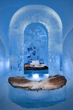 an ice hotel with a bed and fur rugs on the floor in front of it