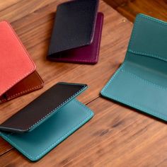 three different colored leather wallets sitting on top of a wooden table next to each other