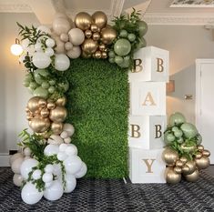 an arrangement of balloons, greenery and letters are arranged on the wall in this baby shower