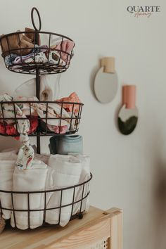 three tiered basket filled with cloths sitting on top of a wooden table next to a wall