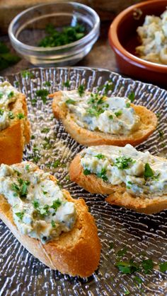 several pieces of bread with various toppings on a glass platter next to bowls