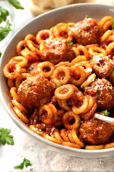 a bowl filled with pasta and meatballs covered in marinara sauce, garnished with parsley