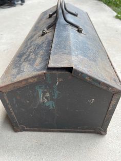 an old metal box sitting on top of a cement floor next to green grass and bushes