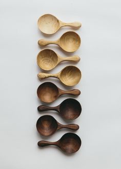 six wooden spoons lined up in a row on a white surface with one empty