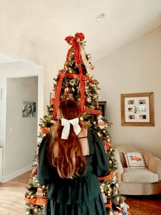 a woman standing in front of a christmas tree with red bows on her head and green dress