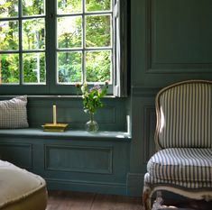 a room with green painted walls and striped chairs in front of a window that looks out onto the woods