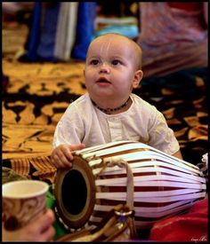 a baby is sitting on the floor playing with a drum and looking up at something