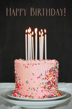 a birthday cake with pink frosting and sprinkles has lit candles on it