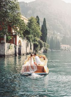 a bride and groom are riding on a boat in the water near some buildings with trees