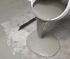 cement being poured into a bucket with a paintbrush on the floor next to it