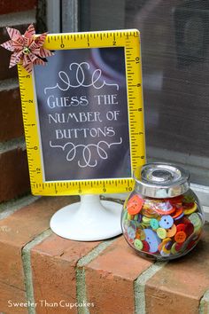 a glass jar filled with buttons next to a sign that says guess the number of buttons