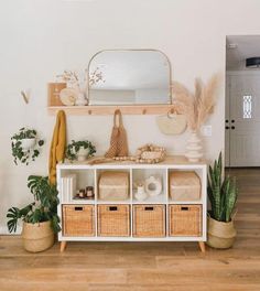 a white shelf with baskets, plants and a mirror on it in a living room