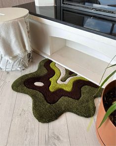 a green and brown rug on the floor in front of a window with a potted plant next to it