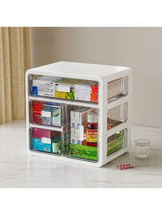 a small white refrigerator with several compartments filled with medicine and other items on the counter