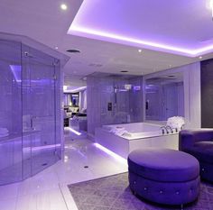 a large bathroom with purple lighting on the ceiling and bathtub in the center, along with a round ottoman