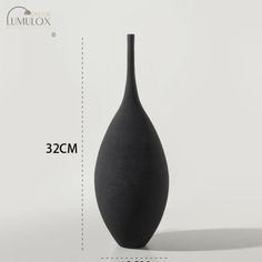 a black vase sitting on top of a white table next to a ruler for measurements