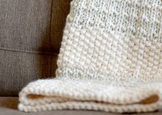 a white knitted blanket sitting on top of a couch