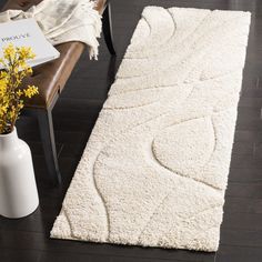 a white rug on the floor next to a chair and vase with flowers in it