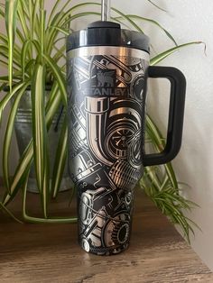 a black and silver travel mug sitting on top of a wooden table next to a potted plant