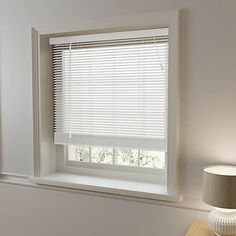 a window with white blinds and a lamp on a table in front of the window